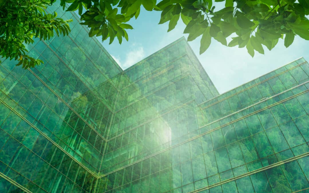 An upward view of a green stretch code building showcasing energy-efficient features can be seen in a modern city. This sustainable glass office building incorporates a tree to reduce heat and utilizes energy-efficient lighting. FreMarq Innovations